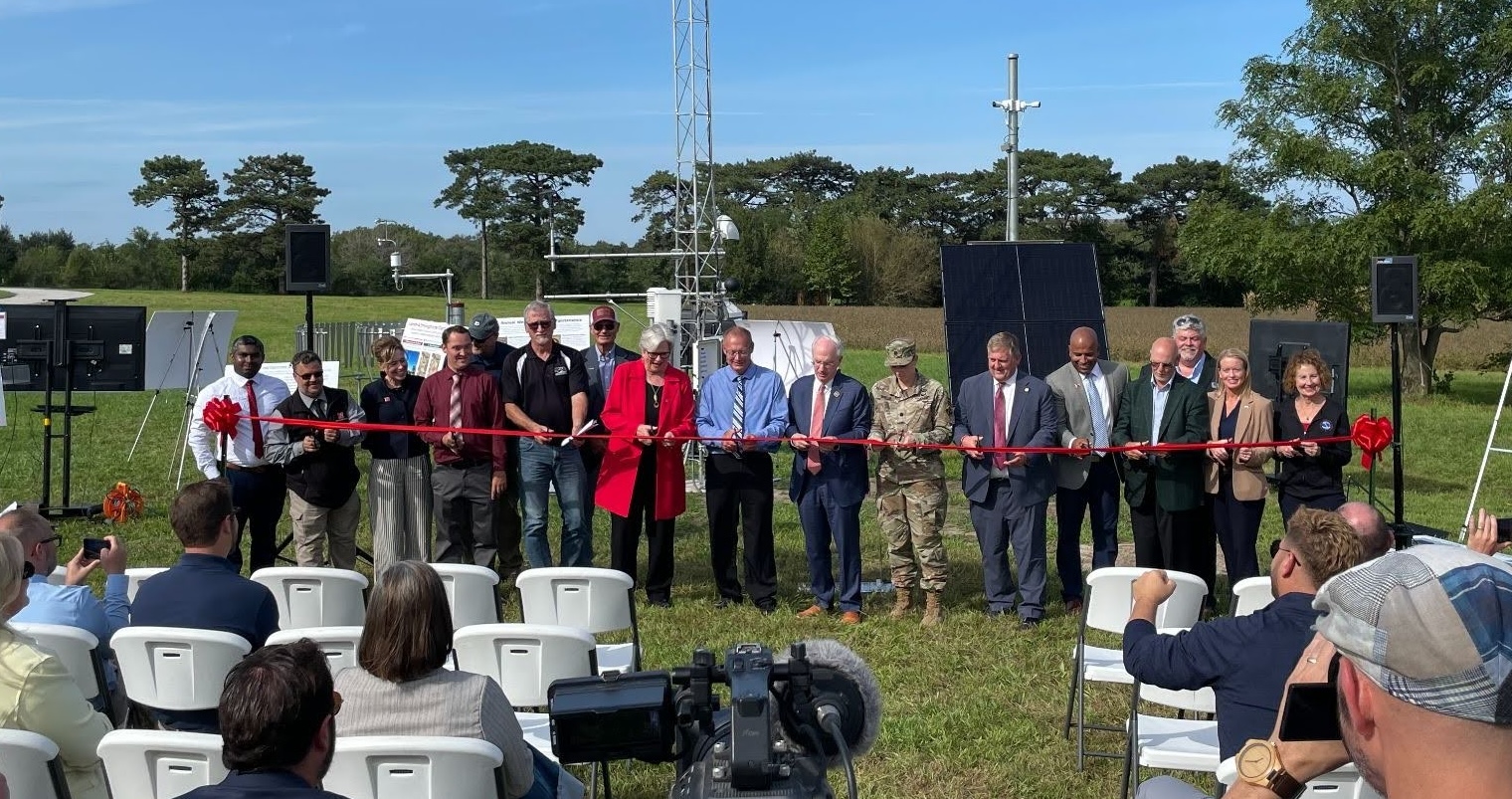 A group of people cutting a red ribbon in front of a crowd, celebrating the new mesonet station installation.
