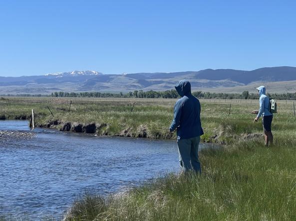 Two anglers on the banks on a Montana river with snow-capped mountains in the background. Photo by the U.S. Geological Survey.