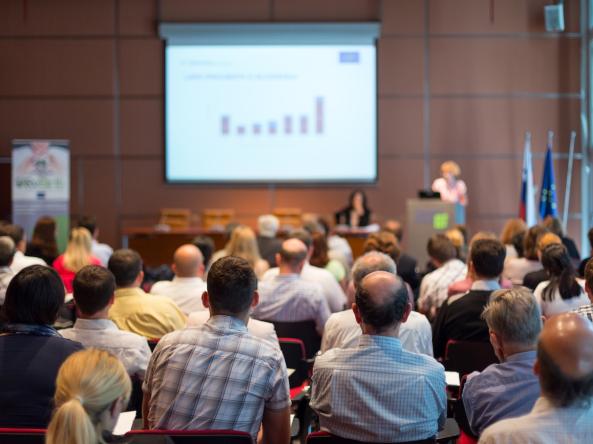 An audience listens to a presentation at a conference. Photo credit: Matej Kastelic, Shutterstock.