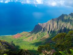 Kauai in Hawaii. A view of the ocean with green grass and shrubs and mountain ridges in the foreground.  Photo credit: Brian Wedekind, Adobe Stock.