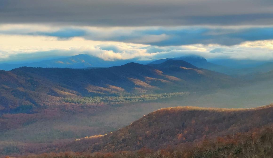 The Smoky Mountains south of Asheville, North Carolina. The mountains are covered in red and orange trees in the fall, with a haze settling over the valley. Photo by Benjamin Kershner on Unsplash.   