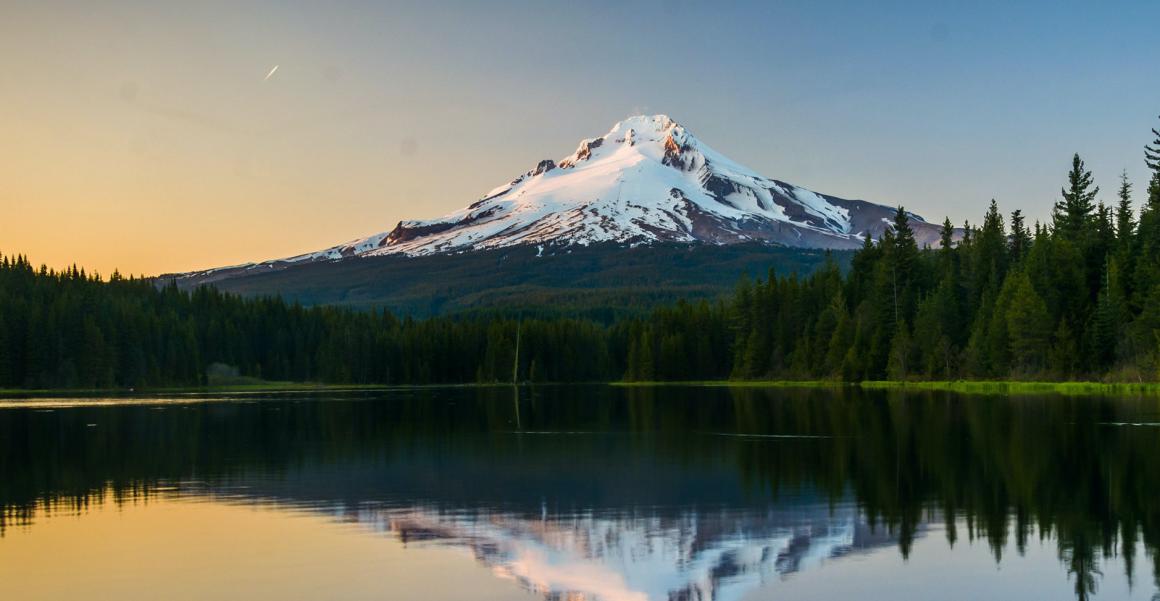 Mount Hood surrounded by water and green trees at sunrise