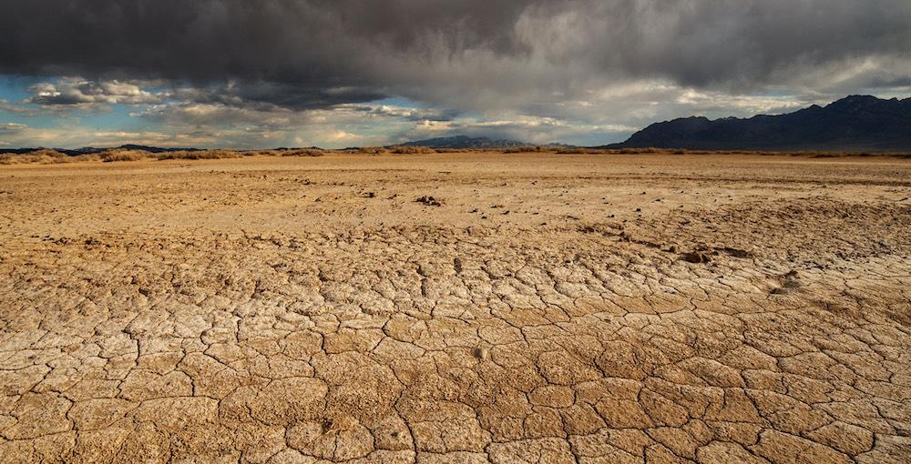 Dry, cracked soil in a Utah desert, with storm clouds rolling in