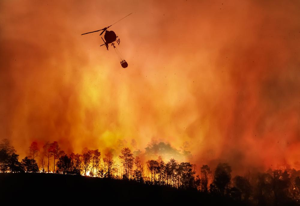 Fire fighting helicopter carrying a water bucket to extinguish a forest fire