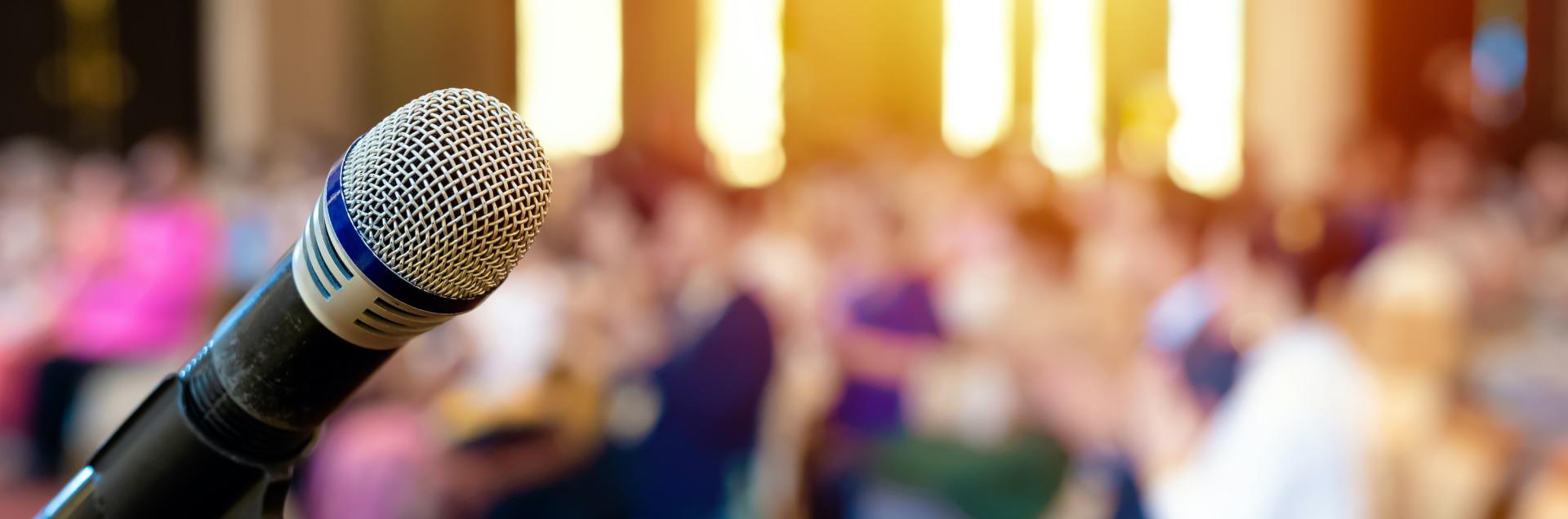 Close up of a microphone on stage with a blurred audience