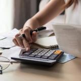 A woman budgets using a calculator. Photo credit: Kittiphan, Adobe Stock.