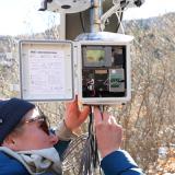 A woman wires into an onset box in a snowy field, representing operations and maintenance. Photo credit: Emilio Matteo, Roaring Fork Observation Network, Aspen Global Change Institute.