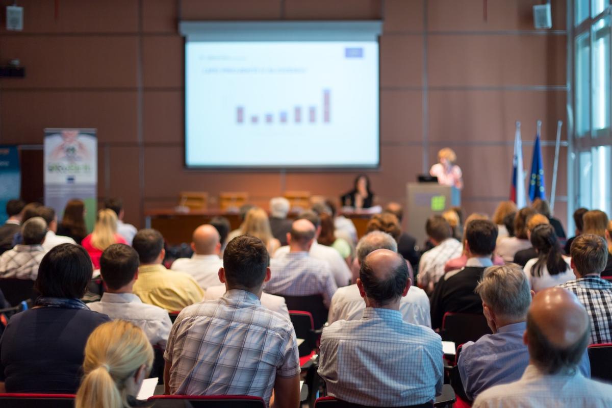 An audience listens to a presentation at a conference. Photo credit: Matej Kastelic, Shutterstock.